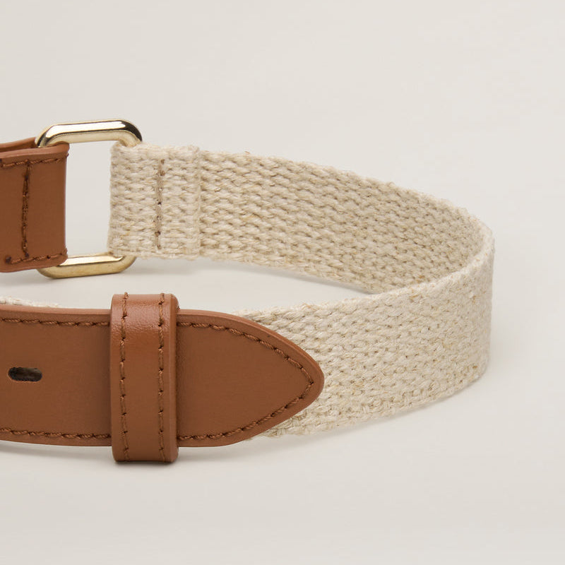 Beige woven belt with brown leather straps on a light beige background