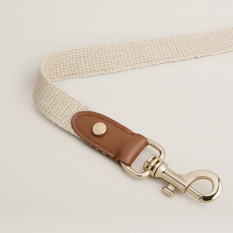Leash with beige strap, brown leather patch, and gold clasp on a light gray background